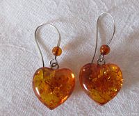 Pair of sterling silver earrings with heart-shaped amber drops and small amber beads on hooks on white fabric background