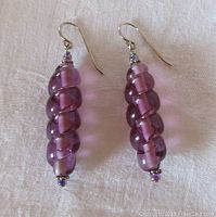 Pair of long drop earrings, twisted purple Lucite with sterling silver hooks and accents, shown on white background.