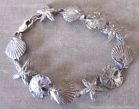Top view of vintage sterling silver bracelet with starfish, scallop shell, and sand dollar charms laid flat, showing clasp and textured details.