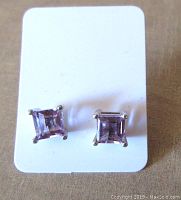 Front view of pair of square amethyst stud earrings on white card, showing light purple gemstones in sterling silver setting.