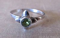 Front-focused photo of the sterling silver ring with a bright green round peridot gemstone set in a bezel with star-like silver framing.