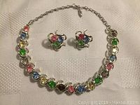 Photo of Coro jewelry set with multicolor rhinestone necklace and matching clip-on earrings laid on white textured fabric.