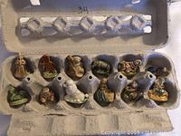 Set of 11 vintage tea figurines displayed in a recycled egg carton, showing different animals and characters in various poses.