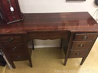 Full front view of vintage wooden desk with six drawers and brass drawer pulls, smooth polished top surface visible.