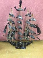 Front view of the large ship sculpture showing three masts and stone sails with string rigging against a pink fabric background.