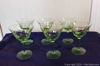 Six green uranium glass cocktail stemware glasses displayed on a blue cloth, showing their green tint and stem shape.