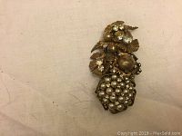 Close-up of front showing cluster of faux pearls and faux diamonds in gold-tone metal forming floral motifs.