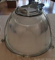 Side view of one glass shade showing ribbed glass and attached metal cage.