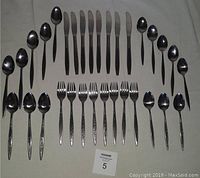 Full set of 32 Japanese stainless steel flatware pieces arranged with 8 forks, 8 knives, 8 tablespoons, and 8 teaspoons. Each piece has black accent patterns on the handles.