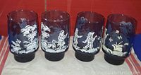 Photo showing four vintage Libbey Mary Gregory glasses with white hand painted children and dog motifs on blue glass, standing upright to display decoration.