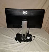 Back view of black Dell monitor showing Dell logo and attached cables coiled at the stand base.