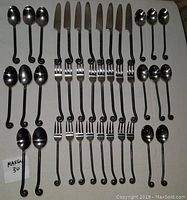Full lot spread with all 40 pieces arranged in rows showing forks, knives and spoons with distinctive curled handles.