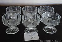 Set of six clear textured glass sherbet or dessert bowls on pedestal bases arranged in two rows on a black fabric backdrop.