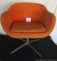 Front view of the mid century swivel chair showing the orange fabric upholstery and the removable seat cushion on a metal base.