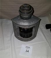 Front view of metal navigation lamp with red glass lens and top chimney ventilation, showing worn and aged condition