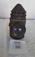 Front view showing fluted top, convex glass lens, and cylindrical rusty metal body of signal lantern.
