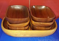 Stacked view of eight smaller teak bowls inside the large oval bowl showing size and shape