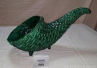 Side angled view of green glazed ceramic cornucopia showing woven texture and three supporting legs.