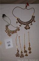 Two sets of costume jewelry necklaces with matching earrings laid out flat showing details, colors, and design.