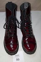 Front view of oxblood high ankle combat boots with laces tied, showing glossy leather and toe cap details.