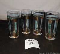 Set of four mid century glasses standing upright on black cloth backdrop, showing blue and gold striped decorative pattern.