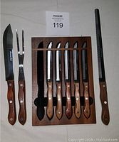 Photo of five Japanese steak knives with wooden handles in wooden block, accompanied by 3-piece carving set with wooden handles (carving knife, fork, sharpening steel). Block has a loose cross piece needing regluing.
