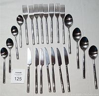 Complete set of 23 pieces of flatware laid out on white background including forks, knives, large spoons and teaspoons with bamboo patterned Inox handles.