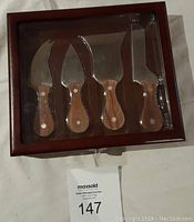 View of entire cheese knife set inside wooden storage case with clear lid, displaying four knives with wooden handles.