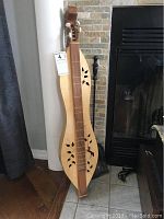 Front view of the 4-string mountain dulcimer showing decorative leaf-shaped sound holes and carved animal motif above lower sound holes.