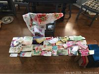 Wide view of multiple folded silk handkerchiefs and a large silk table runner draped over a bench.