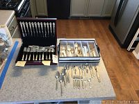 Photo showing complete Wm. Rogers silver-plate set with forks, knives, spoons arranged in a wood display box and loose flatware pieces on countertop