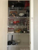 Closet shelving with various Tupperware containers, kitchen tools, and small appliances visible including a blender container and red and white containers with lids.