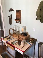 Image showing various vintage items on a metal foldout table including oil lamps, glass jars, small kitchen utensils, an antler-handled basket, and the Electrasteem vaporizer in original box.