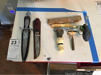 Full view of lot including Korium Pic knife with sheath, three vintage razors, shaving brush, soap brush, and shaving powder dispenser shown on table.