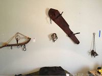 Wide shot of wooden yoke, leather rifle sheath, metal spurs, and decorative chain hung item on wall