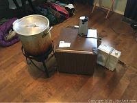 Full lot showing turkey fryer setup with pot on burner, mini fridge with electric can opener on top, and small white fan beside fridge.