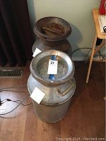 Two metal milk cans, one vintage with rust and embossed marking 'FRUITY-UNION' and the other more contemporary with an aluminum appearance.
