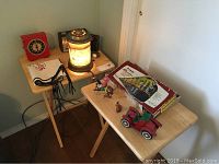 Vintage imaged heating lamp glowing, red square clock, two radios including one with case, and various toys on two wooden tables.