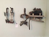 Three pairs of vintage ice skates hung on a wall showing different styles, including one pair of black leather boot skates and two pairs of adjustable metal strap skates.