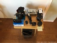 Overview of all items including Ricoh XLR 500 camera with leather case, external flash, light meter, lenses, Konica FF-88 camera with box, Sanyo Micro Talk cassette recorder with box, and leather carrying bag on table.