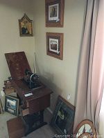 Four framed art pieces displayed near a window and sewing machine, includes golden colored Renaissance replica and wood framed artwork.