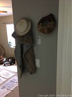 Overall view showing chinchilla stole draped over hanger with beige hat nearby, and a brown fur-trimmed hat with netting mounted on the wall.