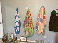 Three vintage handmade baby quilts hanging on a wall, showing different color schemes and patchwork designs.