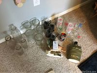 Photo showing full collection of glass items on carpet including branded glasses, milk bottles, and Jim Beam bottles