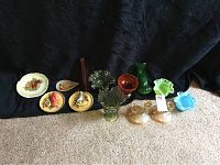 Photo showing 3 glass candleholders, 3 glass vases in green, amber, and blue tones, several small decorative plates and bird-themed ceramic items arranged on dark fabric background