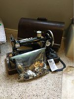 Antique Singer sewing machine in original wooden case with a bag of assorted buttons and spools of thread placed in front.