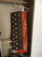 Two silk Japanese obis hanging on a rack, one black with small flowers, one orange with large floral hexagonal pattern.