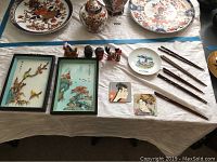 A collection of Japanese decorative items including framed wall art, small figurines, chopsticks, and small plates arranged on white cloth.