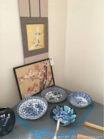 Two pieces of wall art and four ceramic bowls arranged on a table corner, showing different patterns and colors.