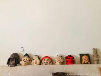 Seven Japanese masks including one mounted mask and varied designs, displayed on a couch.